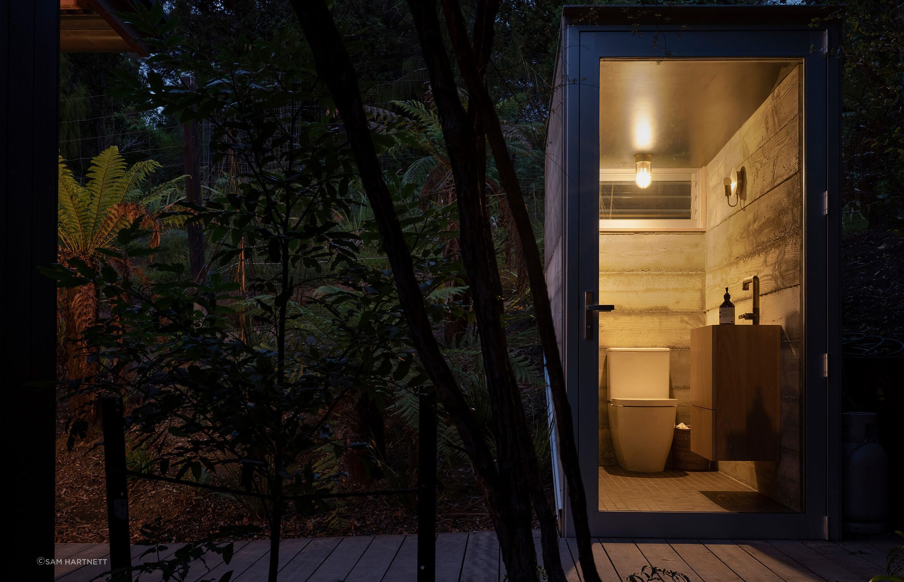 A timber boardwalk leads further uphill to a semi-buried toilet, hunkered into the land with concrete and framed by a fully glazed frontage.