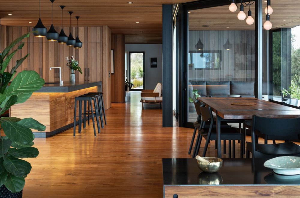 The cedar ceiling and recycled rimu flooring mirror each other, giving way to black accents of the aluminium joinery, exposed concrete, and other finer details.