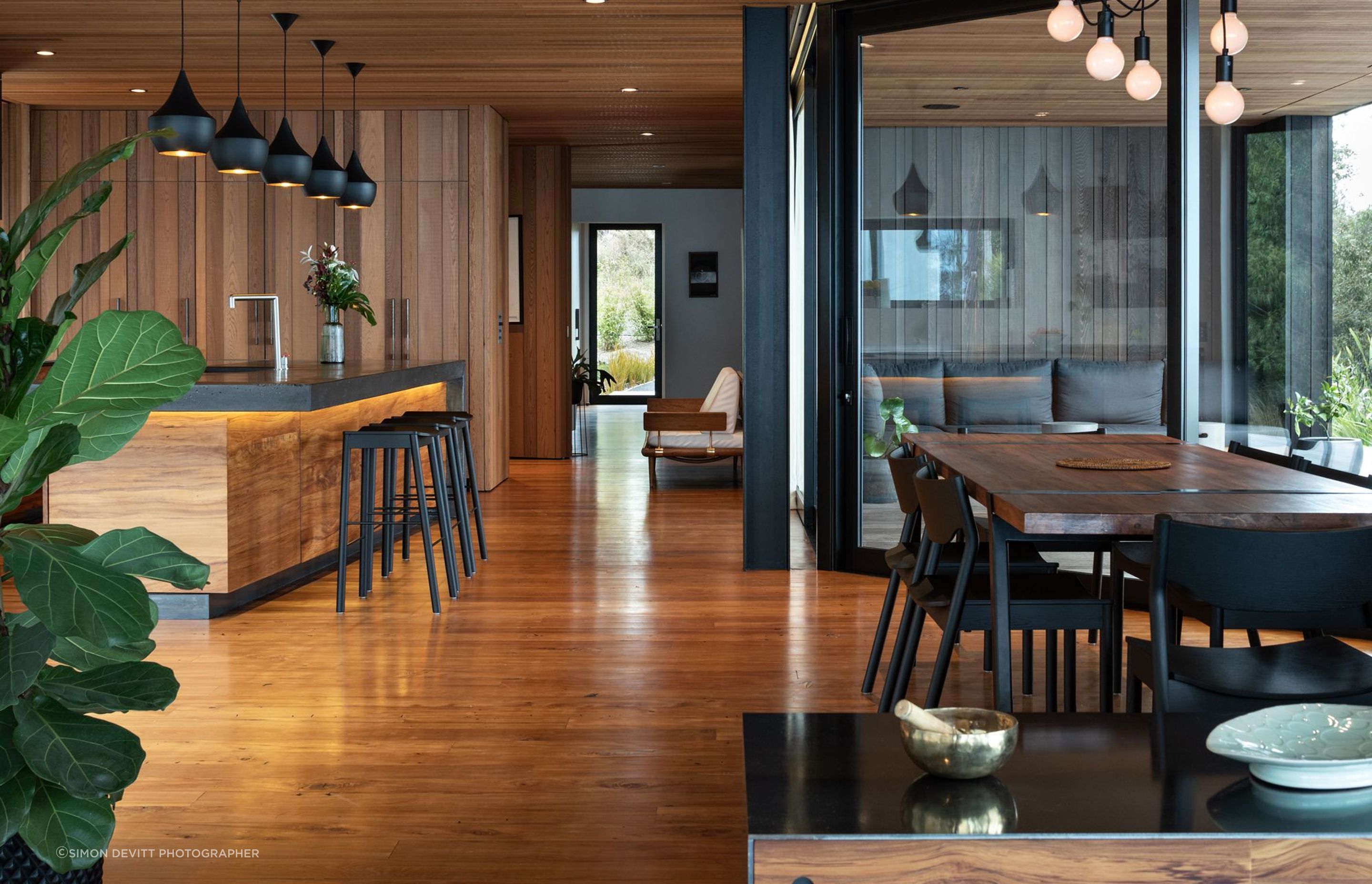 The cedar ceiling and recycled rimu flooring mirror each other, giving way to black accents of the aluminium joinery, exposed concrete, and other finer details.