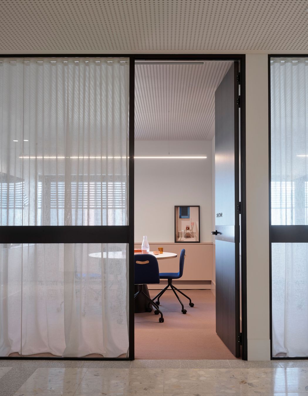 A meeting room is softened with pastel colours, sheer curtains and beautiful photographic art.