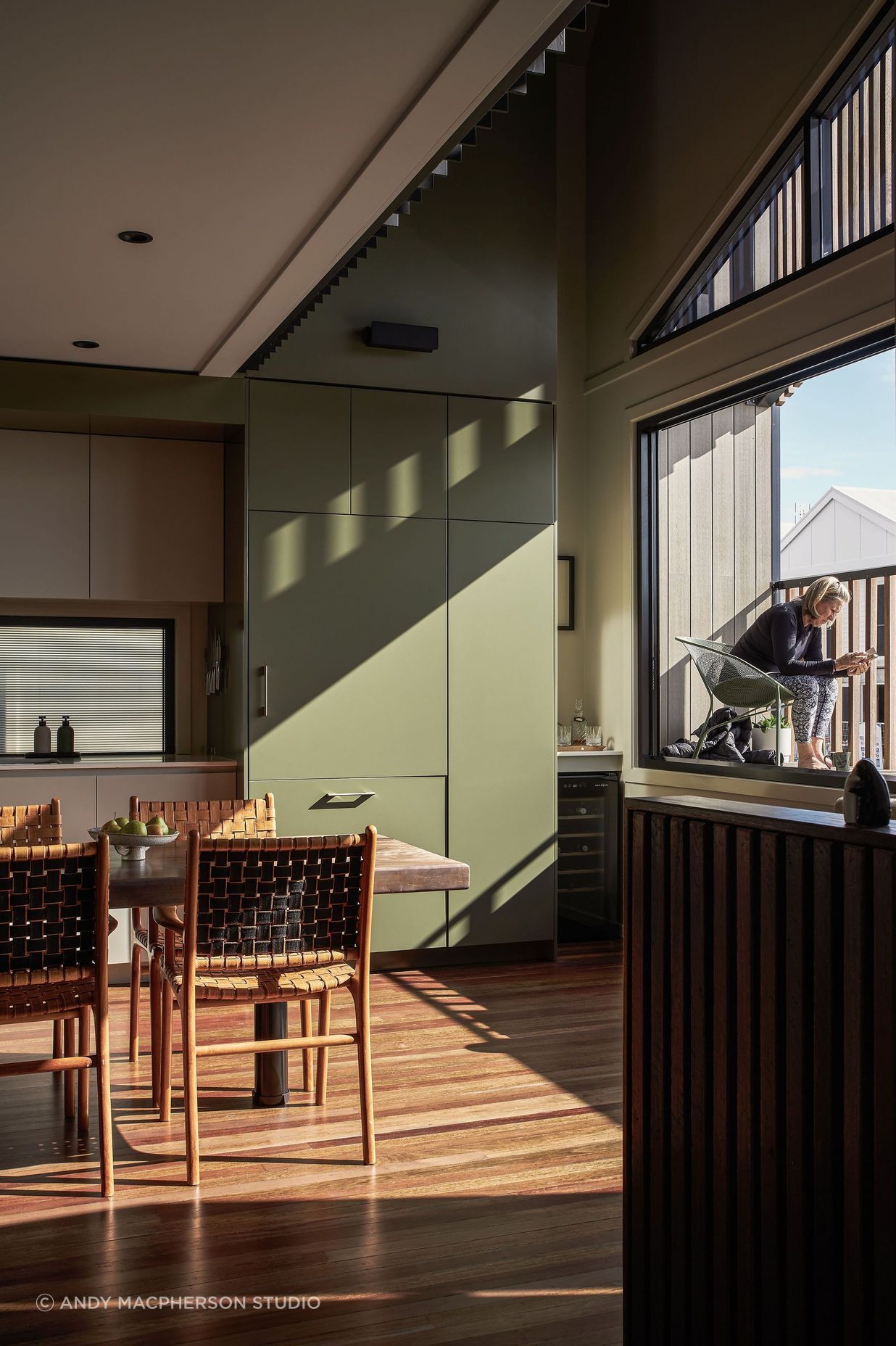 The palette features soft hues of sage and pale greens paired with natural timbers. To the right of the kitchen, a small balcony overlooks the street, capturing the morning and midday sun as it’s filtered through the timber batten screen.