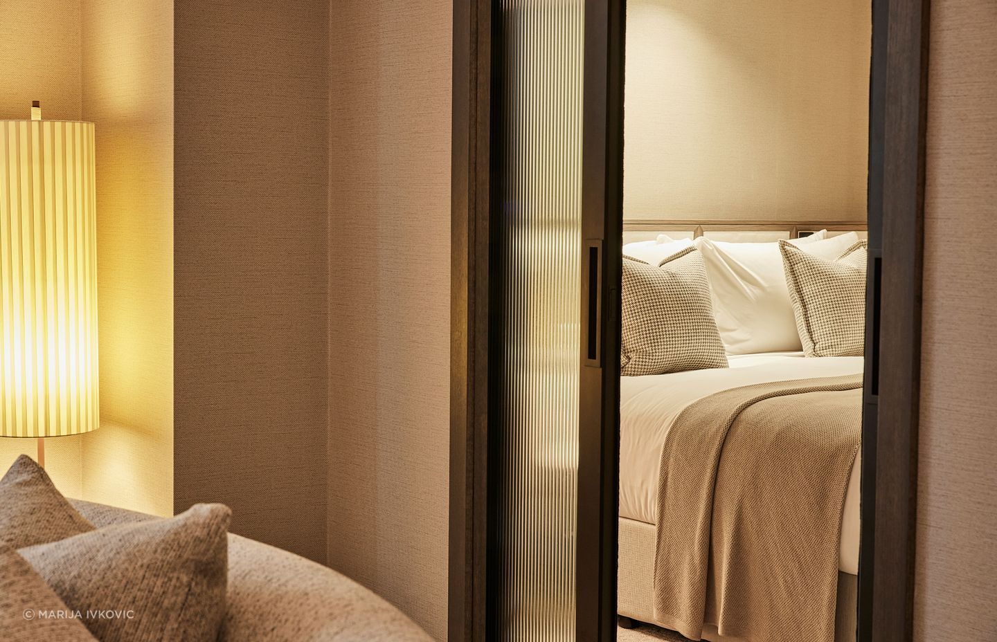 Fluted glass sliders give a bedroom privacy from the main living space in a suite; the textured wallpaper softens the space and adds a textural richness.