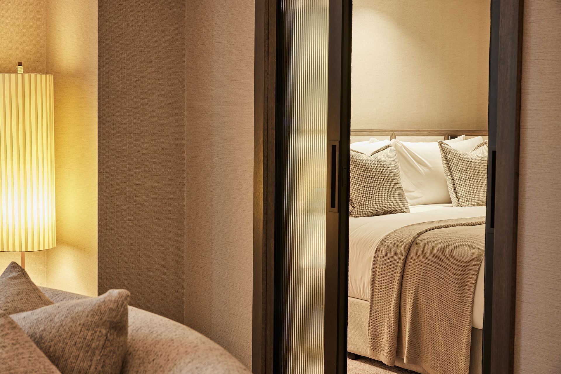 Fluted glass sliders give a bedroom privacy from the main living space in a suite; the textured wallpaper softens the space and adds a textural richness.
