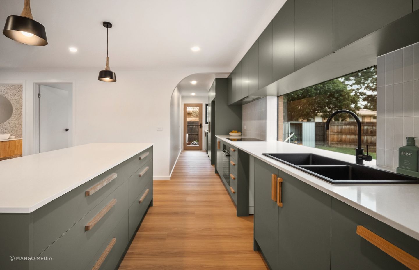 An earthy green defines the kitchen, with an arch leading to the laundry area.