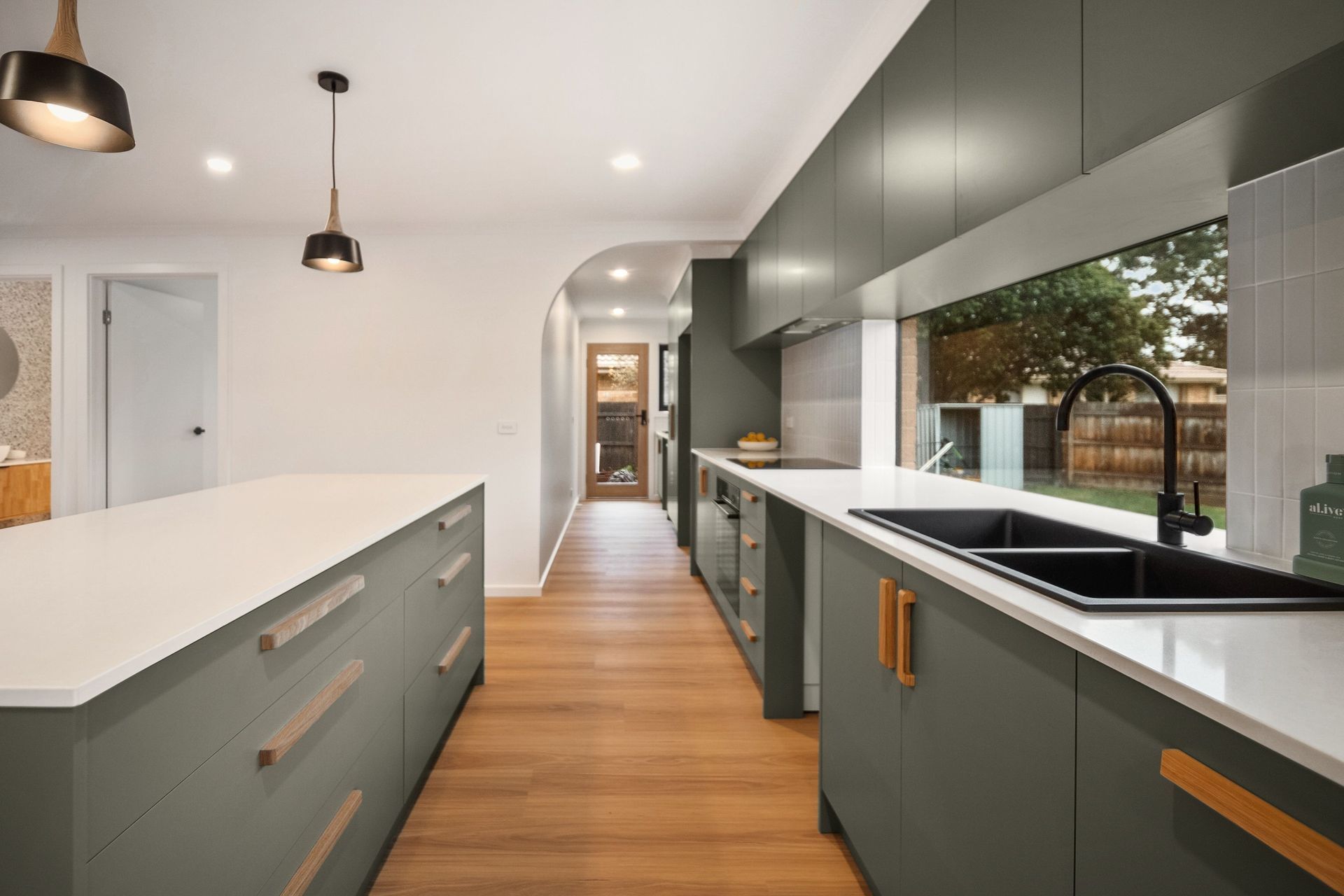 An earthy green defines the kitchen, with an arch leading to the laundry area.