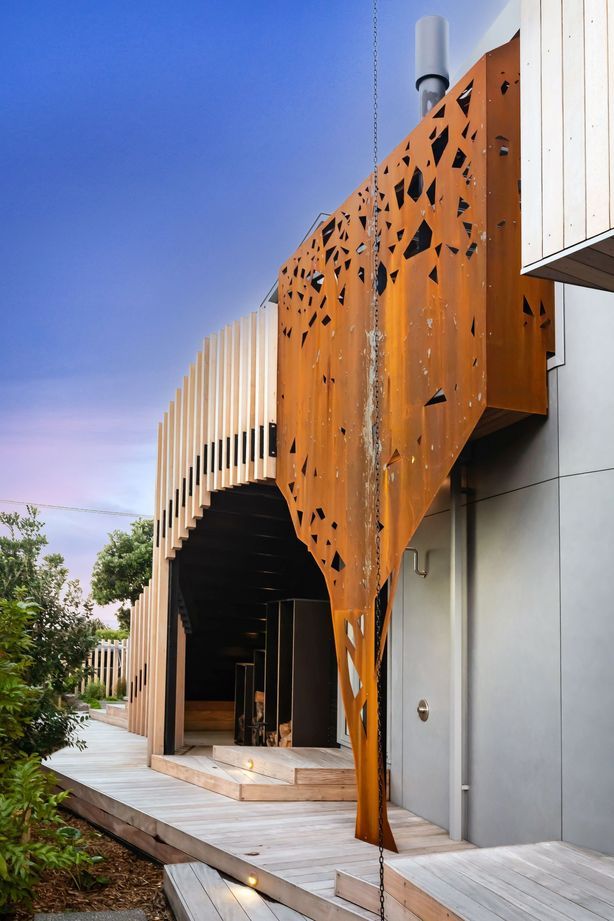 Wrapping around the outdoor fireplace, corten steel has been formed to mimic the silhouette of a pōhutukawa tree across the road from the house.