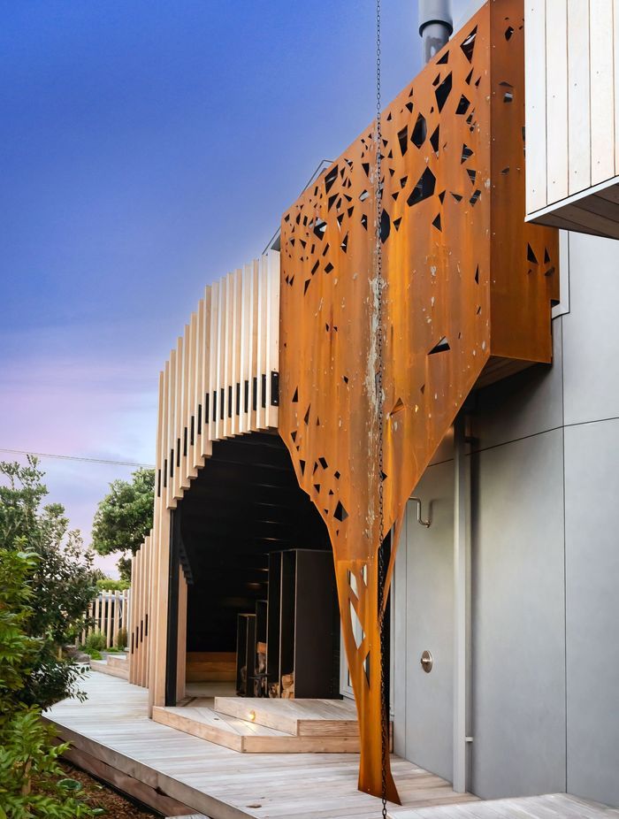 Wrapping around the outdoor fireplace, corten steel has been formed to mimic the silhouette of a pōhutukawa tree across the road from the house.