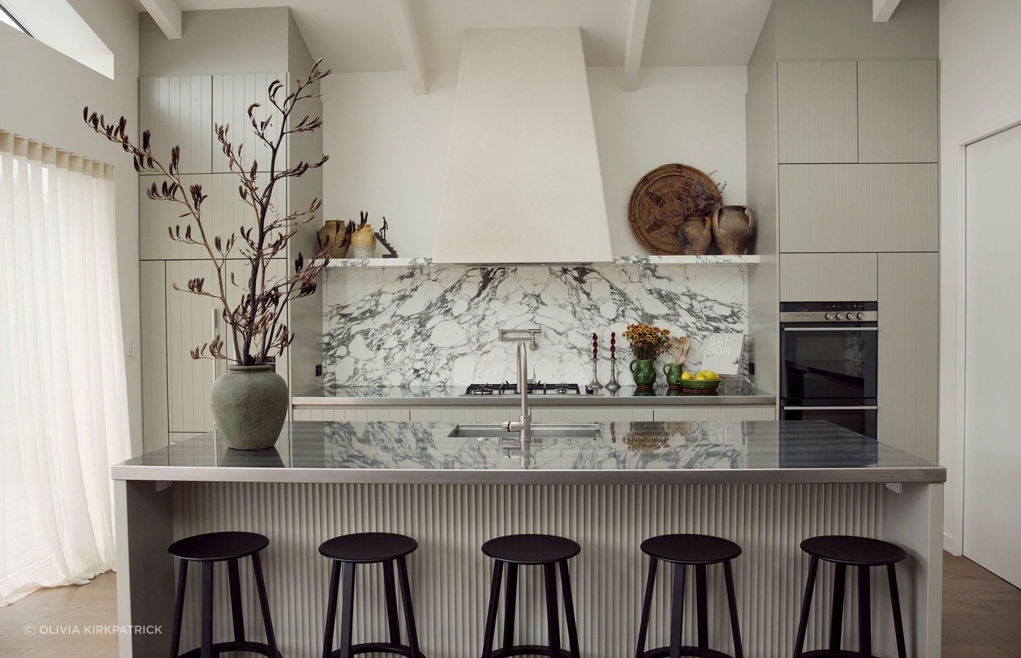 With appliances and storage relegated to the walls, a large island bench offers space for food prep and casual meals without cutting communication between the chef and others using the space.