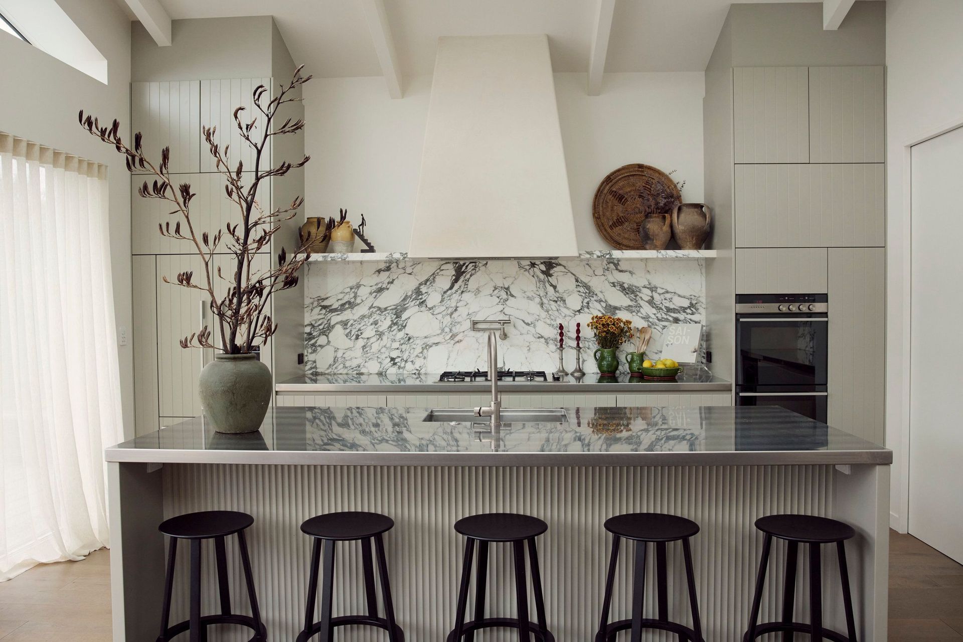 With appliances and storage relegated to the walls, a large island bench offers space for food prep and casual meals without cutting communication between the chef and others using the space.