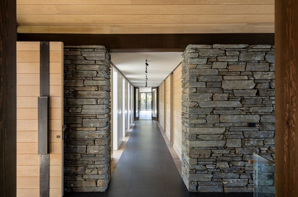 On both sides of the entry, a schist-clad wall anchors the home, with hallways leading to the bedrooms on the left, and living spaces on the right.