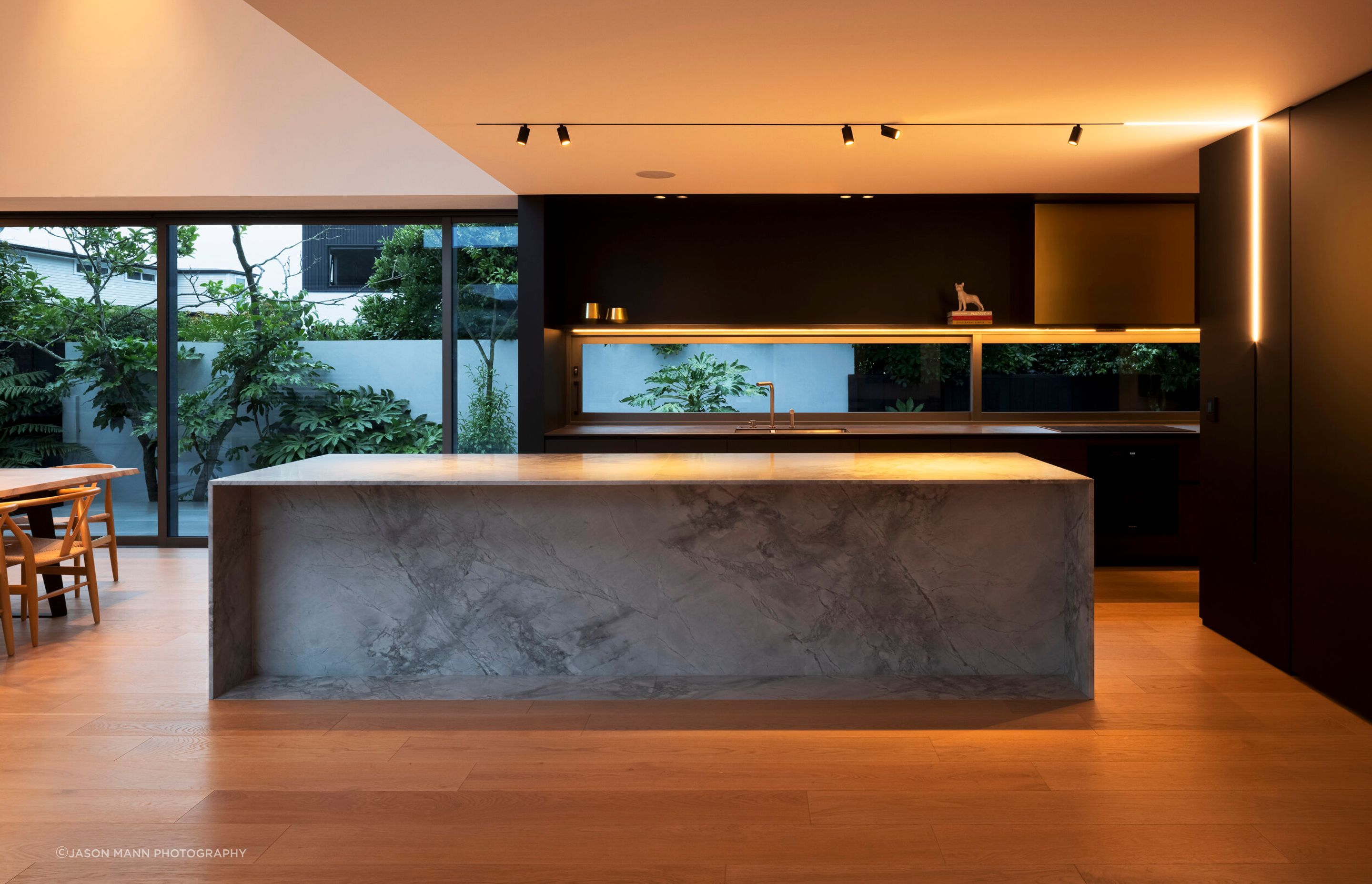 The kitchen is centrally positioned in the flattened 'T' shape arrangement, spilling into two living areas with distinct spatial experiences.