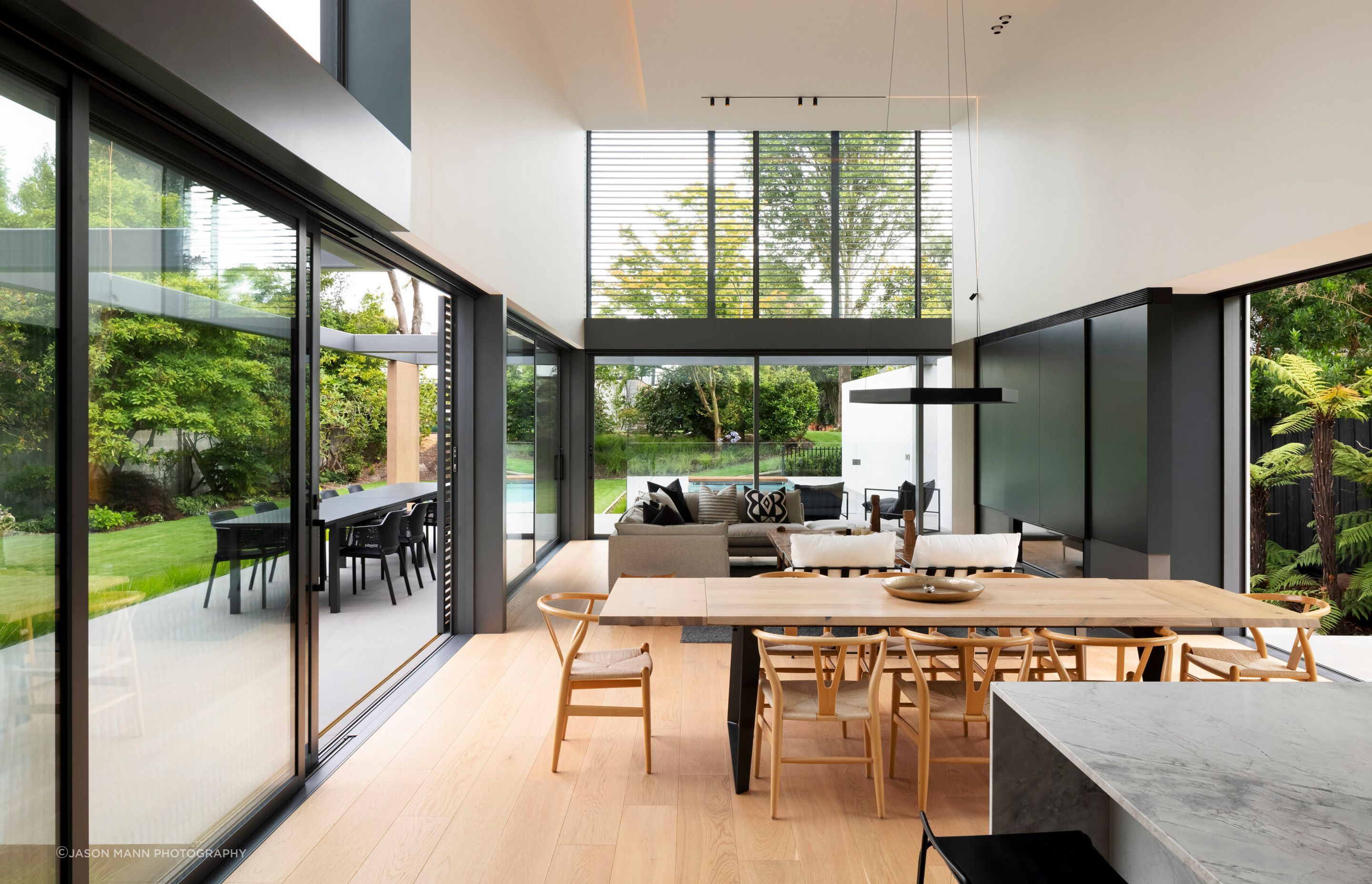 The first living area is an expansive, double-height space. The sightline naturally flows through the large sliding doors towards 180-degree views of the established garden and pool.