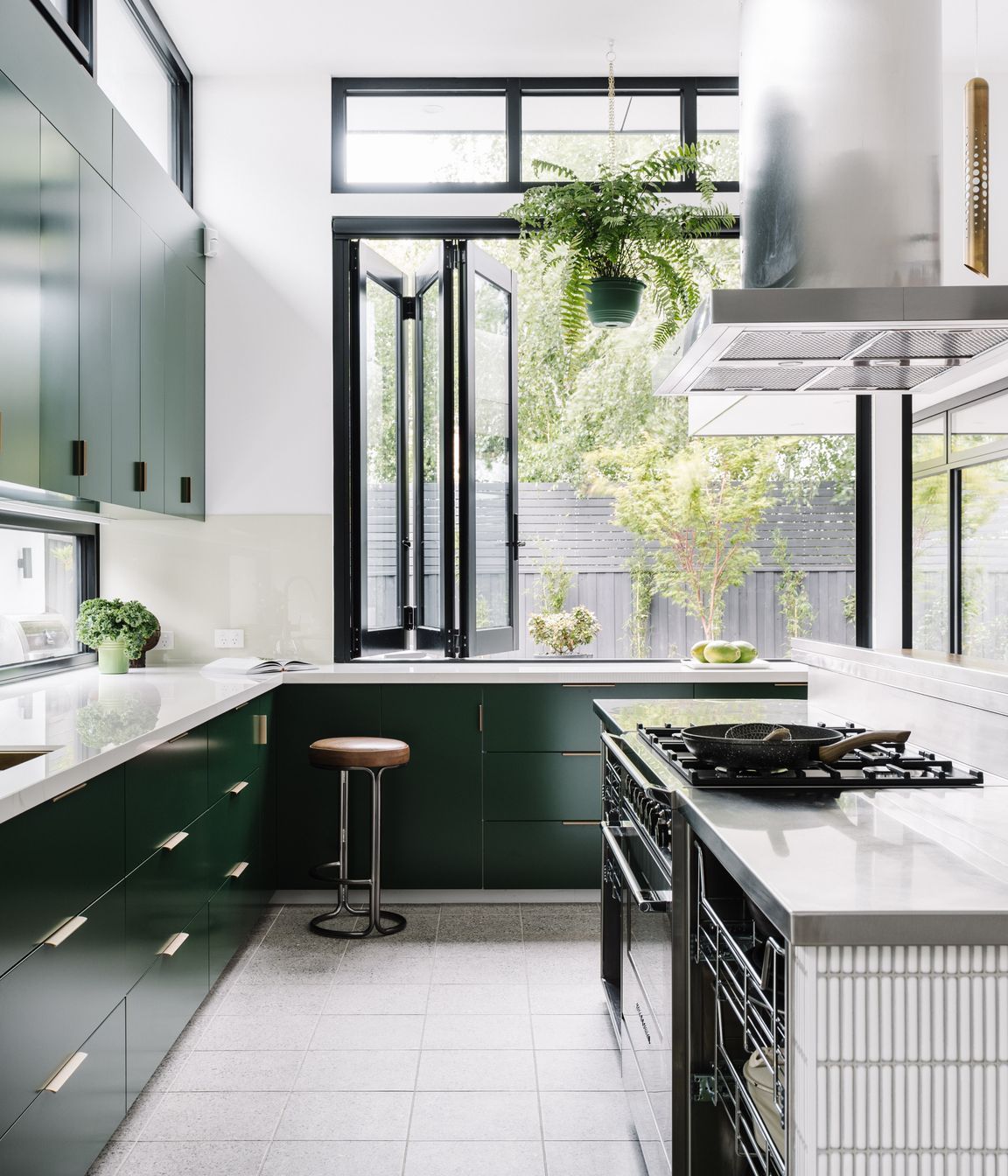 The kitchen island workspace is stainless steel with custom steel rack draws providing easy access to pots and pans. The rest of the joinery is 2pac dark green with a Dekton glacier benchtop.