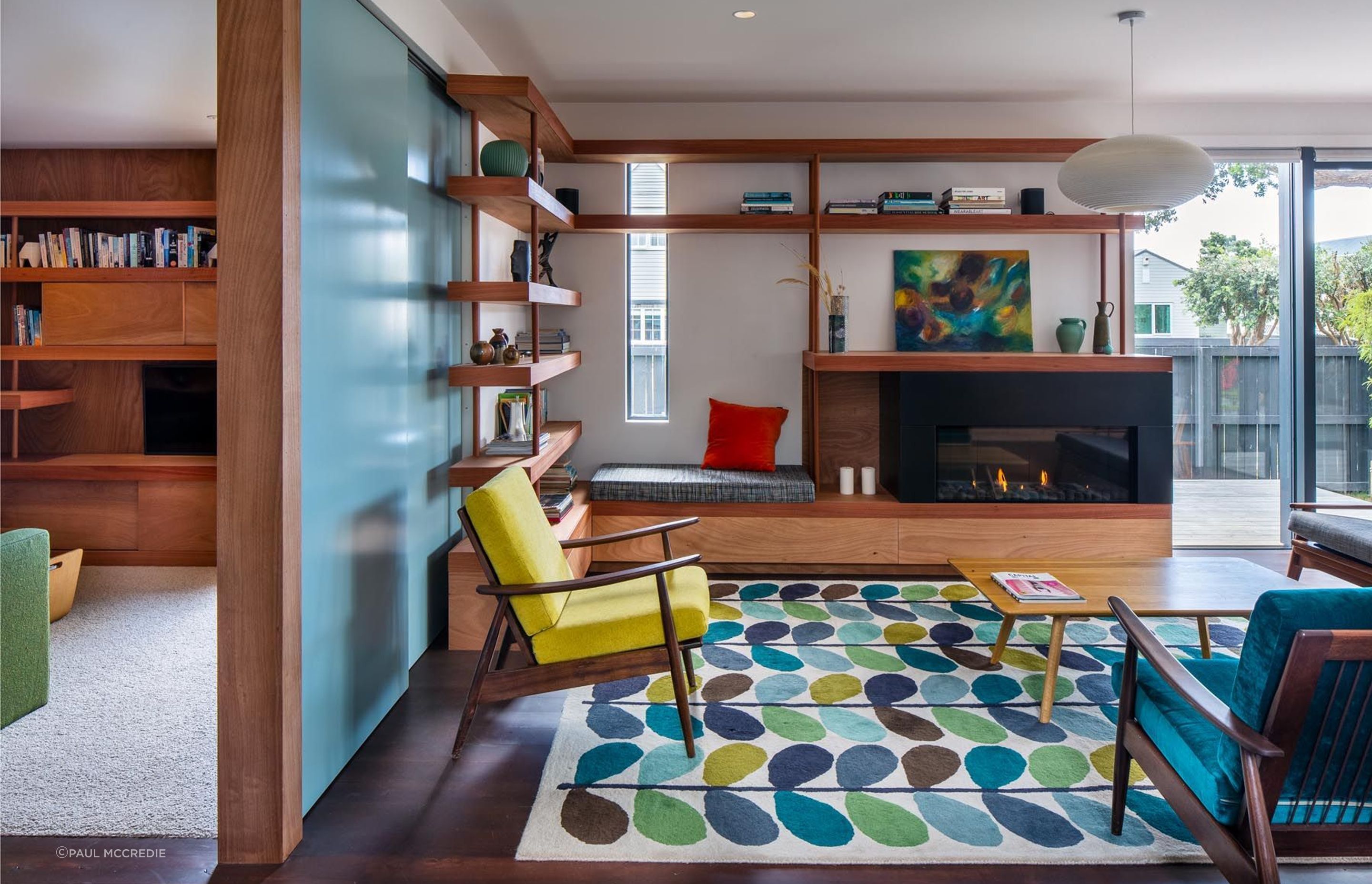 The built-in window seat is one of many options in the house for a sunny spot to sit. Sturdy timber shelving adds weight to the room, and the clients helped choose the mid-century furnishings.