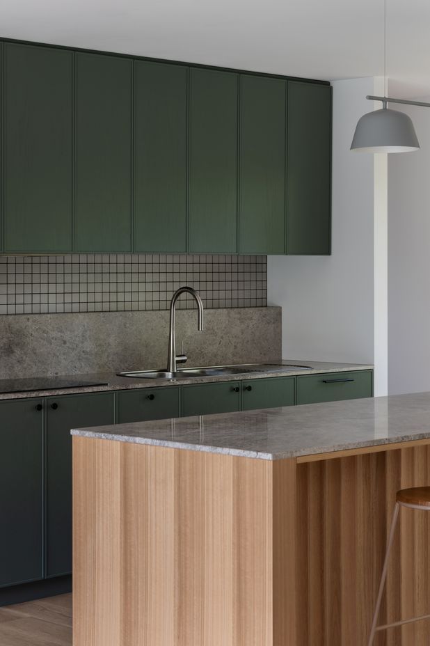 The bottle green kitchen talks to the nearby framed greenery.