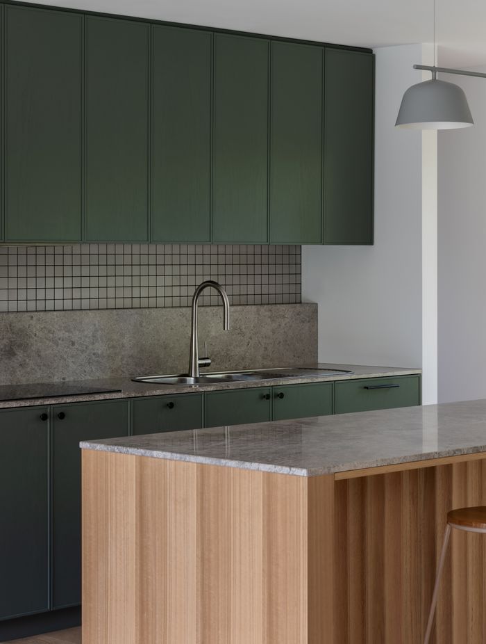 The bottle green kitchen talks to the nearby framed greenery.