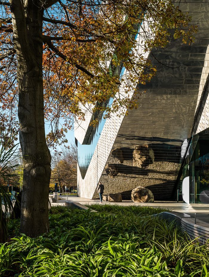 The mirrored façade reflects the patterned pavers at the building's entrance.