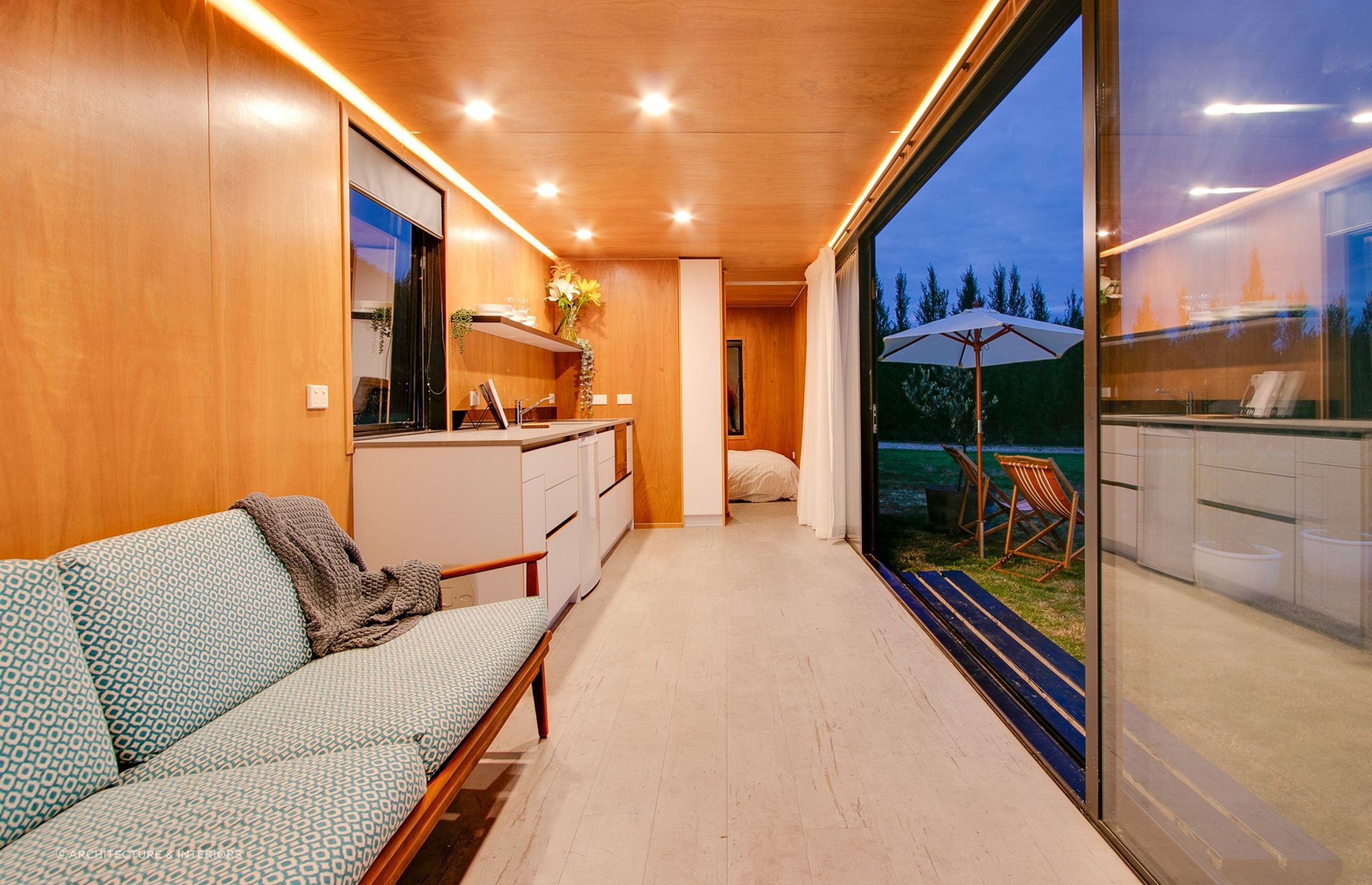 An interior clad with red plywood and strong recessed and strip lighting add great warmth to this shipping container home