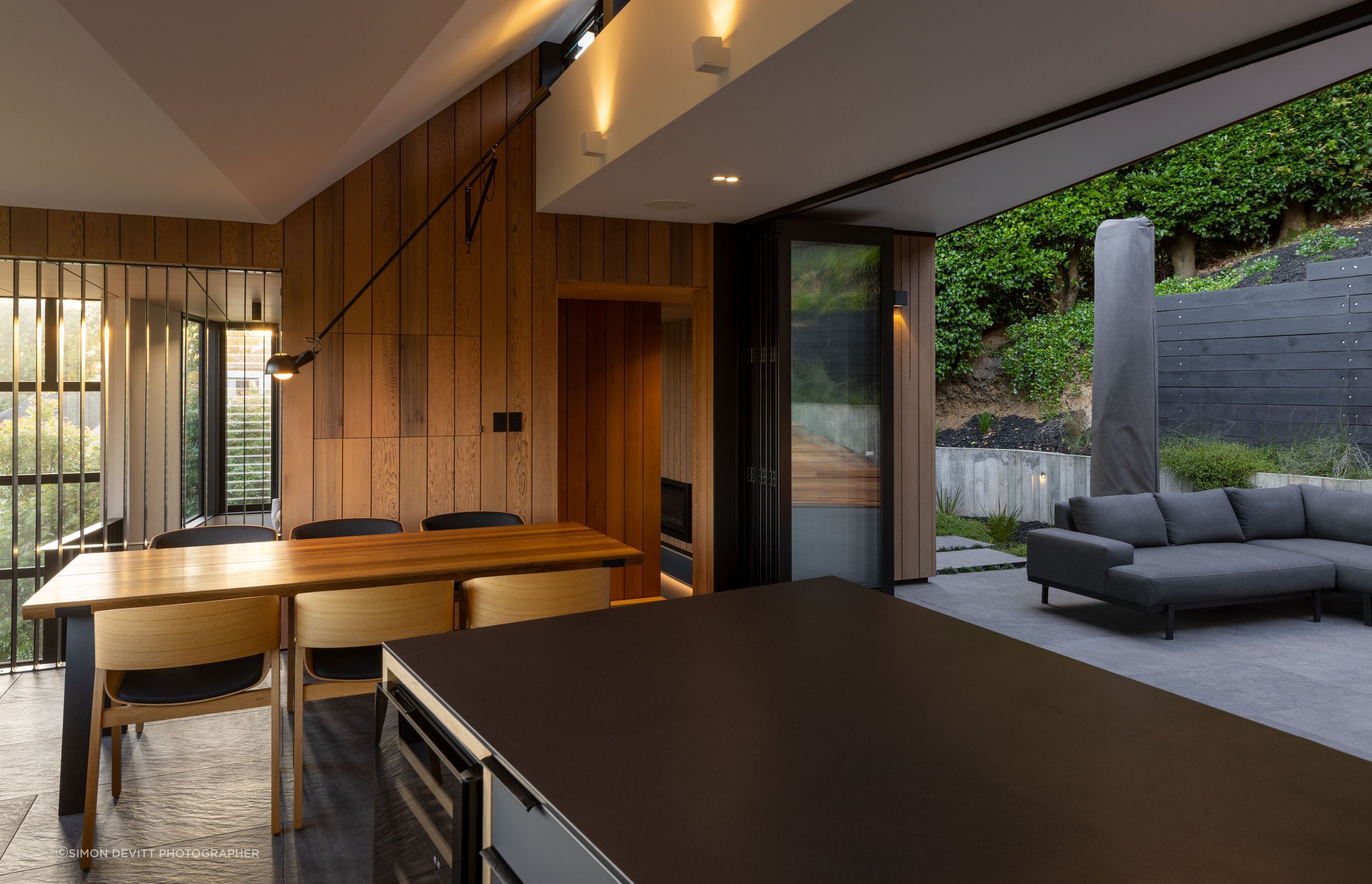 An interior open-plan kitchen and dining area flows seamlessly into an exterior space.