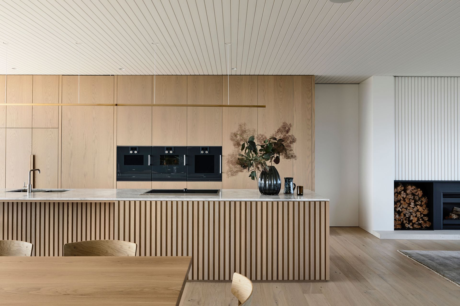 The kitchen, dining and lounge space are open-plan, and are integrated through timber panelling and a pale, cohesive palette of white and timber.