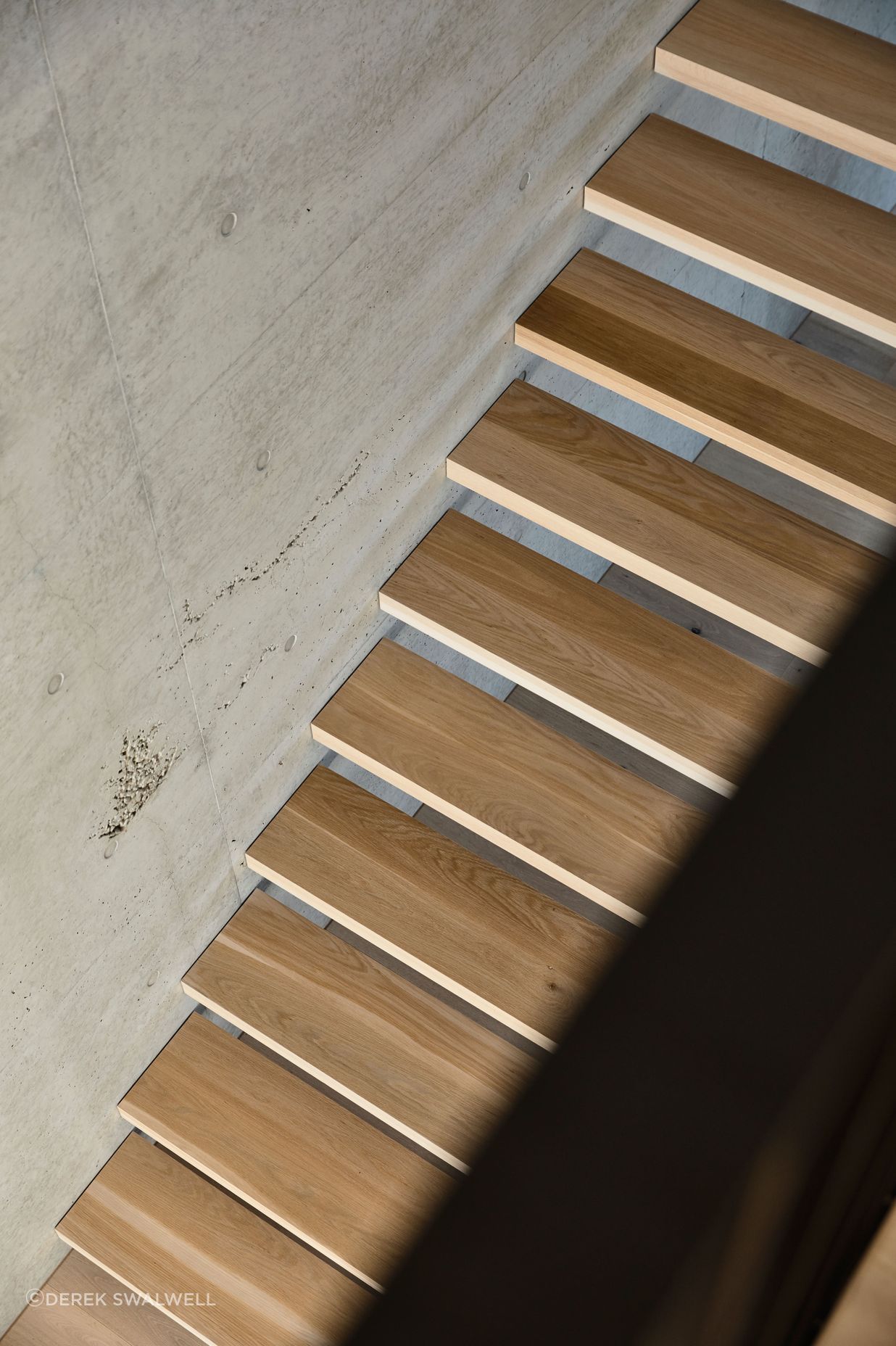 Elegant timber treads contrast against the tactile concrete wall.