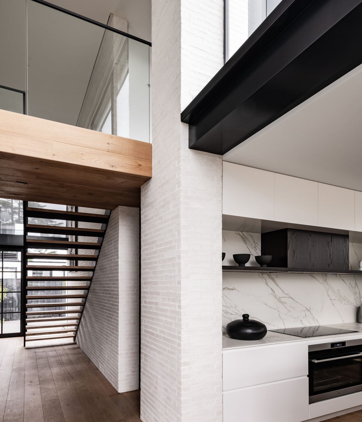 The bridge at the top of the stairs leads to two bedroom suites, and a powder room is tucked underneath. Glazing over the kitchen brings light into the double height living room.