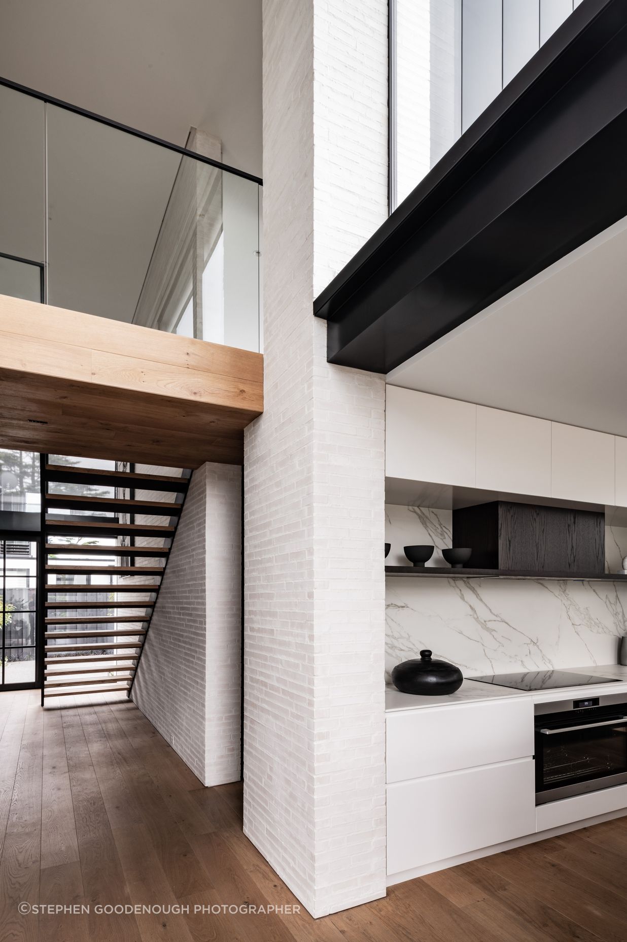 The bridge at the top of the stairs leads to two bedroom suites, and a powder room is tucked underneath. Glazing over the kitchen brings light into the double height living room.