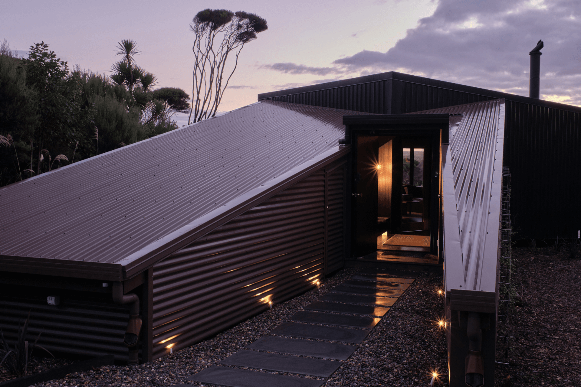 Upon arrival, the home is low to the land, consisting of one brown structure and one black, which lean to meet one another. The brown structure is split to create a protective passageway to the entry.