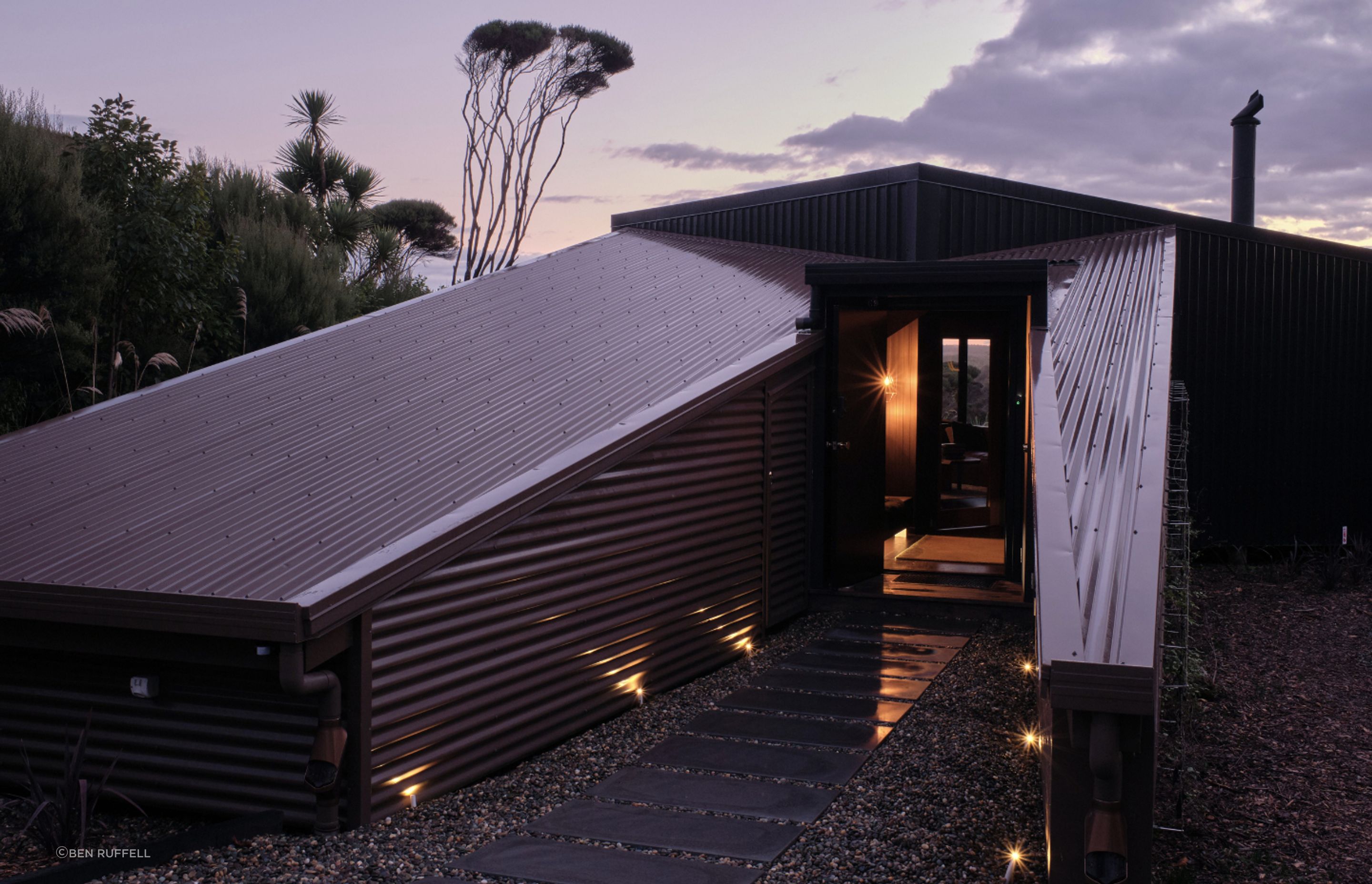 Upon arrival, the home is low to the land, consisting of one brown structure and one black, which lean to meet one another. The brown structure is split to create a protective passageway to the entry.