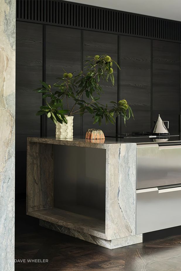 The stainless steel Shape kitchen by Poliform features a tapered cut and sleek integrated handles, perfectly complementing the marble columns that anchor the kitchen island.