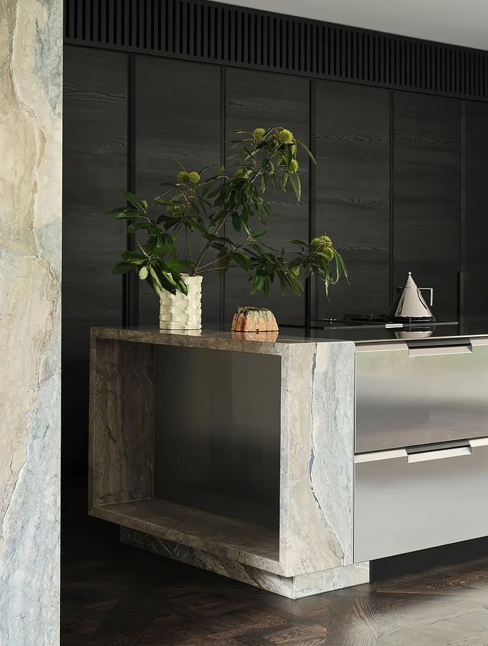 The stainless steel Shape kitchen by Poliform features a tapered cut and sleek integrated handles, perfectly complementing the marble columns that anchor the kitchen island.
