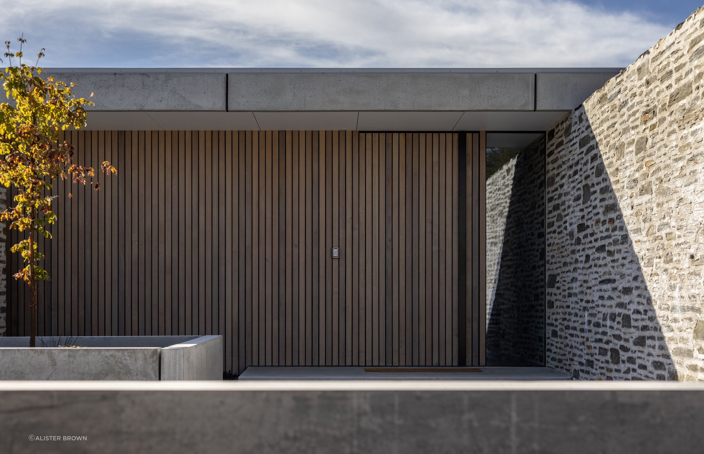 A schist stone wall guides visitors toward the entry.