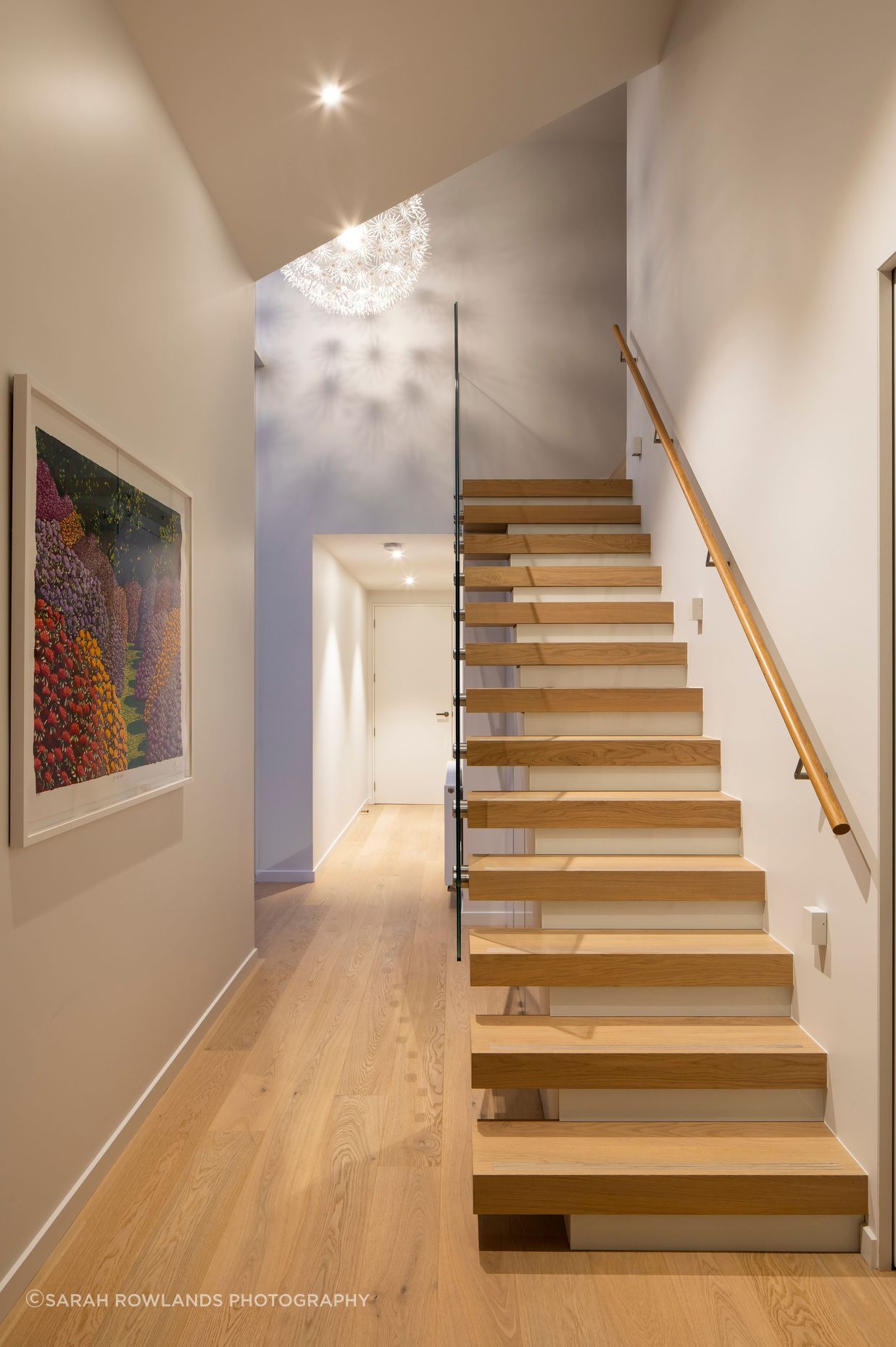 A floating staircase leads to the upper-storey master bedroom suite, while the hallway leads to secondary bedrooms, a bathroom and garage.