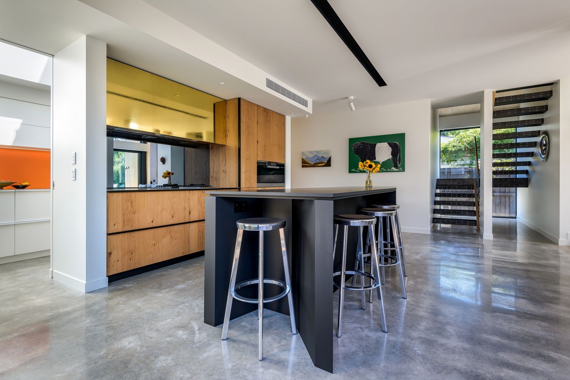 Looking west from the kitchen to the staircase.  Timber cabinetry is accented by a mirrored glass splashback that reflects the outdoor fire and the mature trees in the garden.