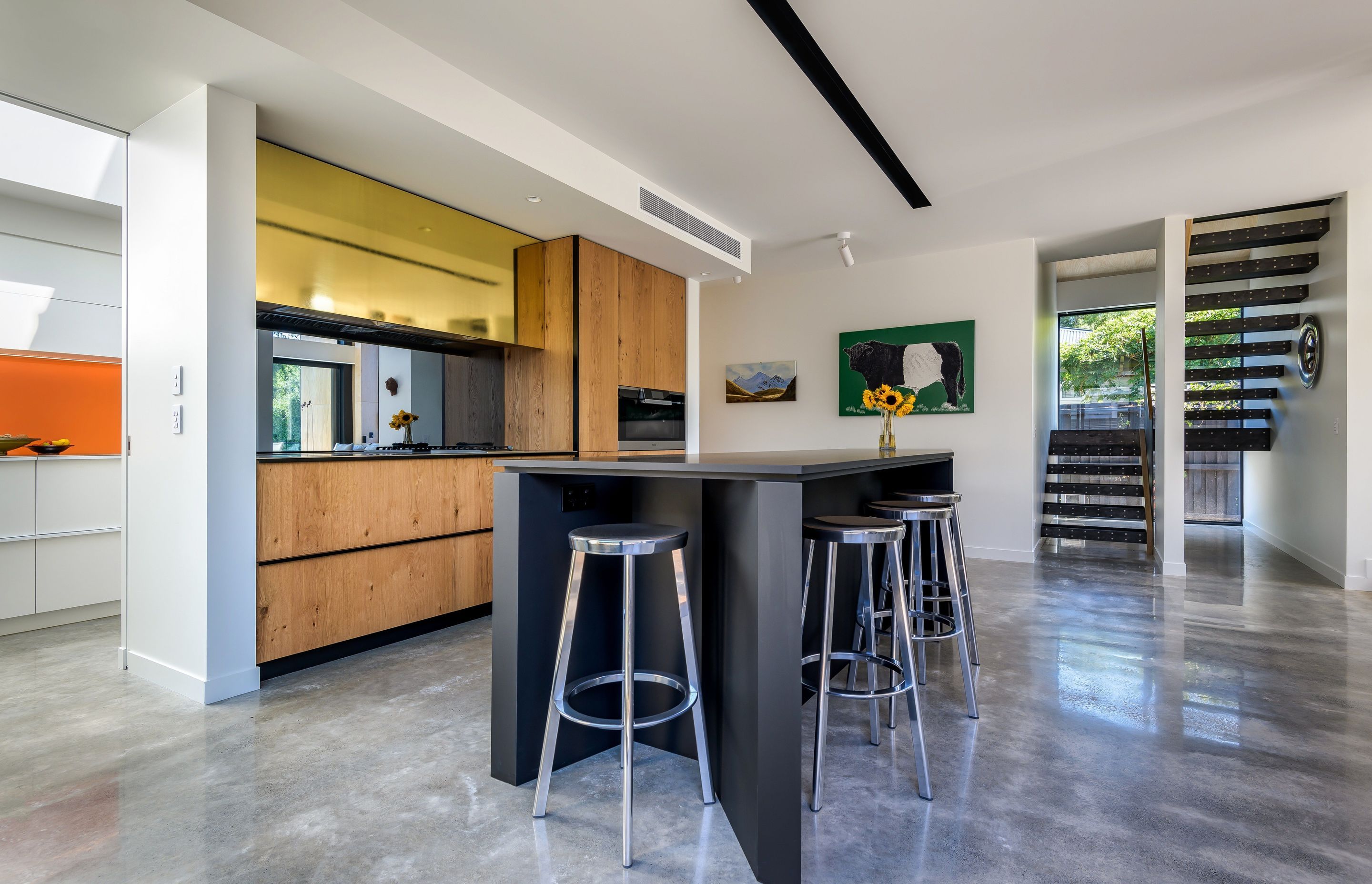 Looking west from the kitchen to the staircase. Timber cabinetry is accented by a mirrored glass splashback that reflects the outdoor fire and the mature trees in the garden.