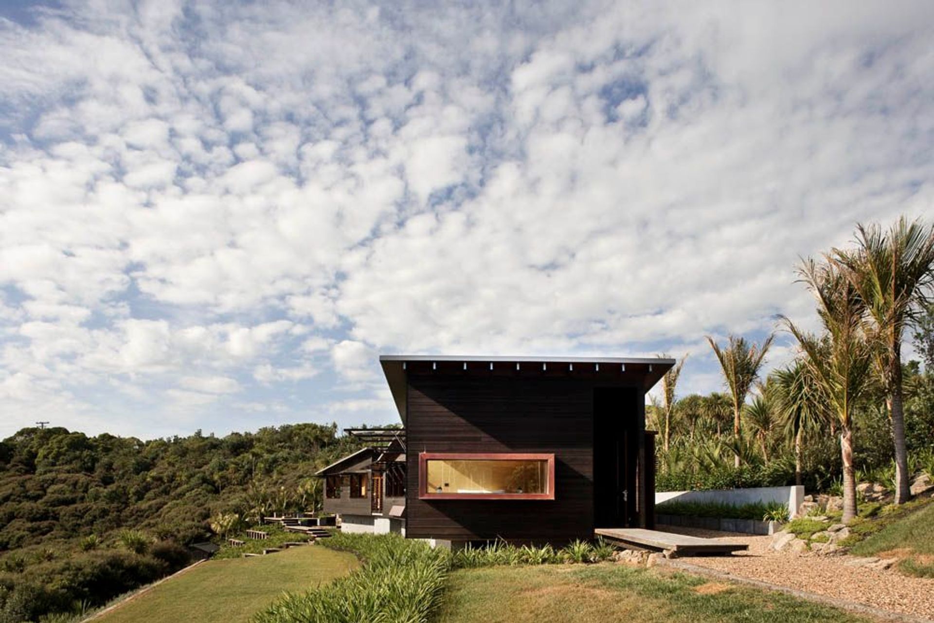 Owhanake Bay house utilises horizontal weatherboards in a dark stain, drawing it lower to the ground and making it recessive in its bush location. By Strachan Group Architects. Photo by Patrick Reynolds.