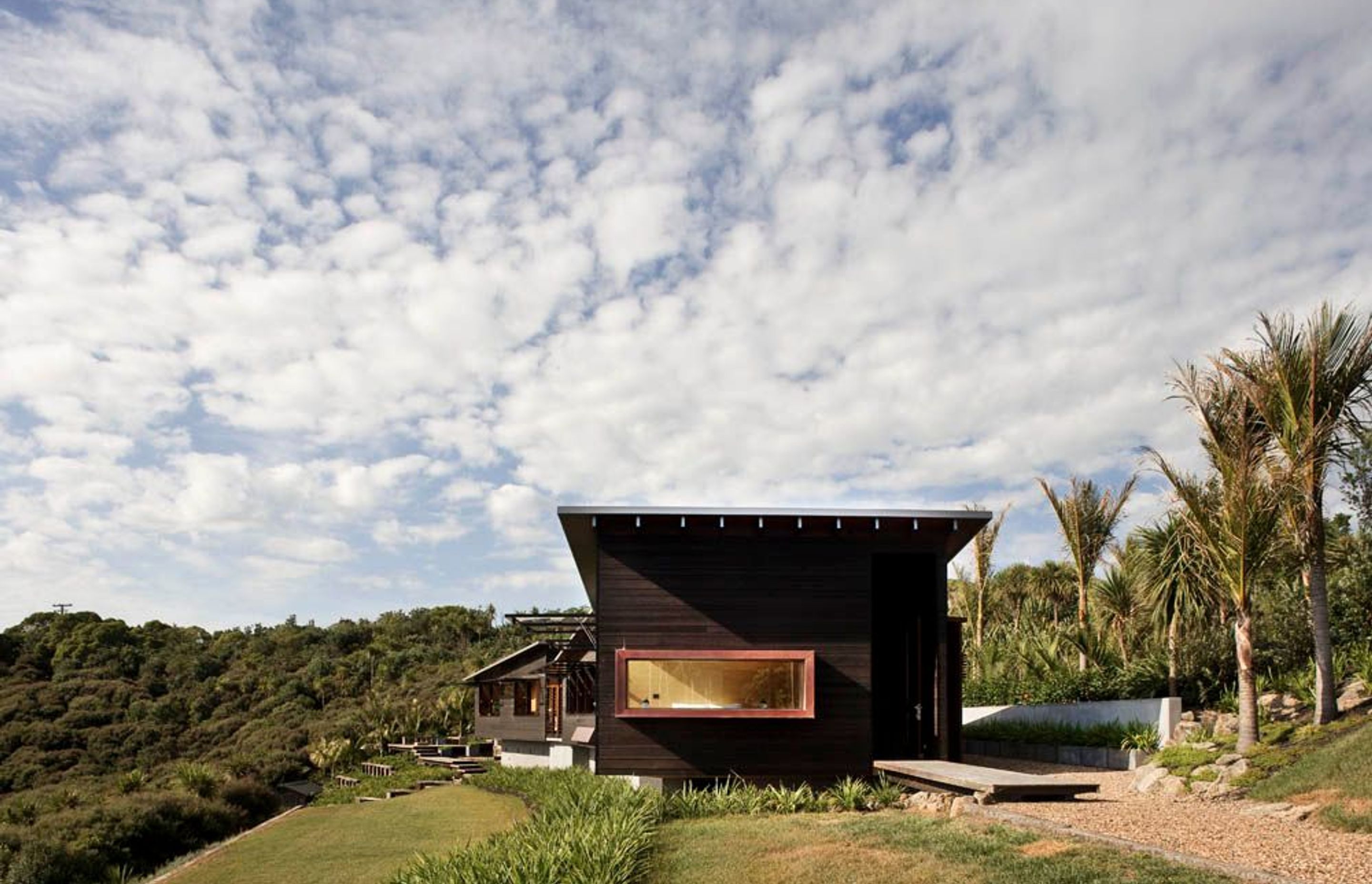 Owhanake Bay house utilises horizontal weatherboards in a dark stain, drawing it lower to the ground and making it recessive in its bush location. By Strachan Group Architects. Photo by Patrick Reynolds.