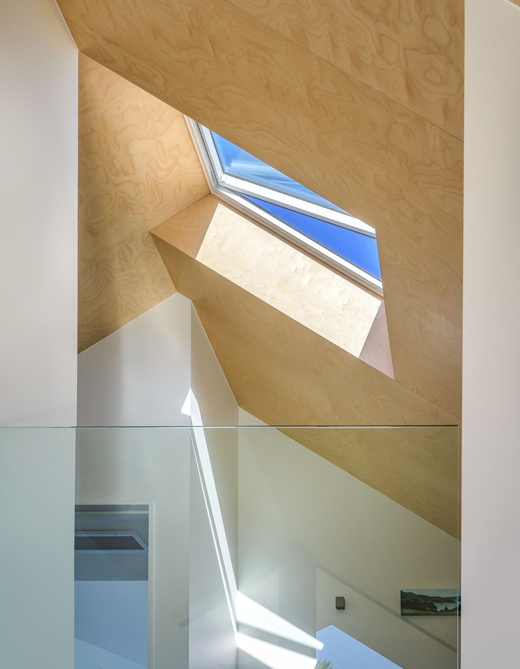 At the top of stairs, the glass balustrade looks down on the living area, north through double-height windows to the trees and swimming pool.