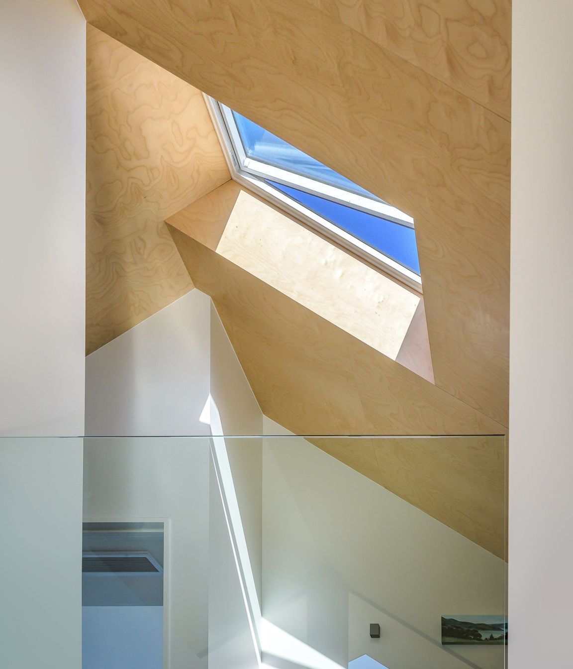 At the top of stairs, the glass balustrade looks down on the living area, north through double-height windows to the trees and swimming pool.
