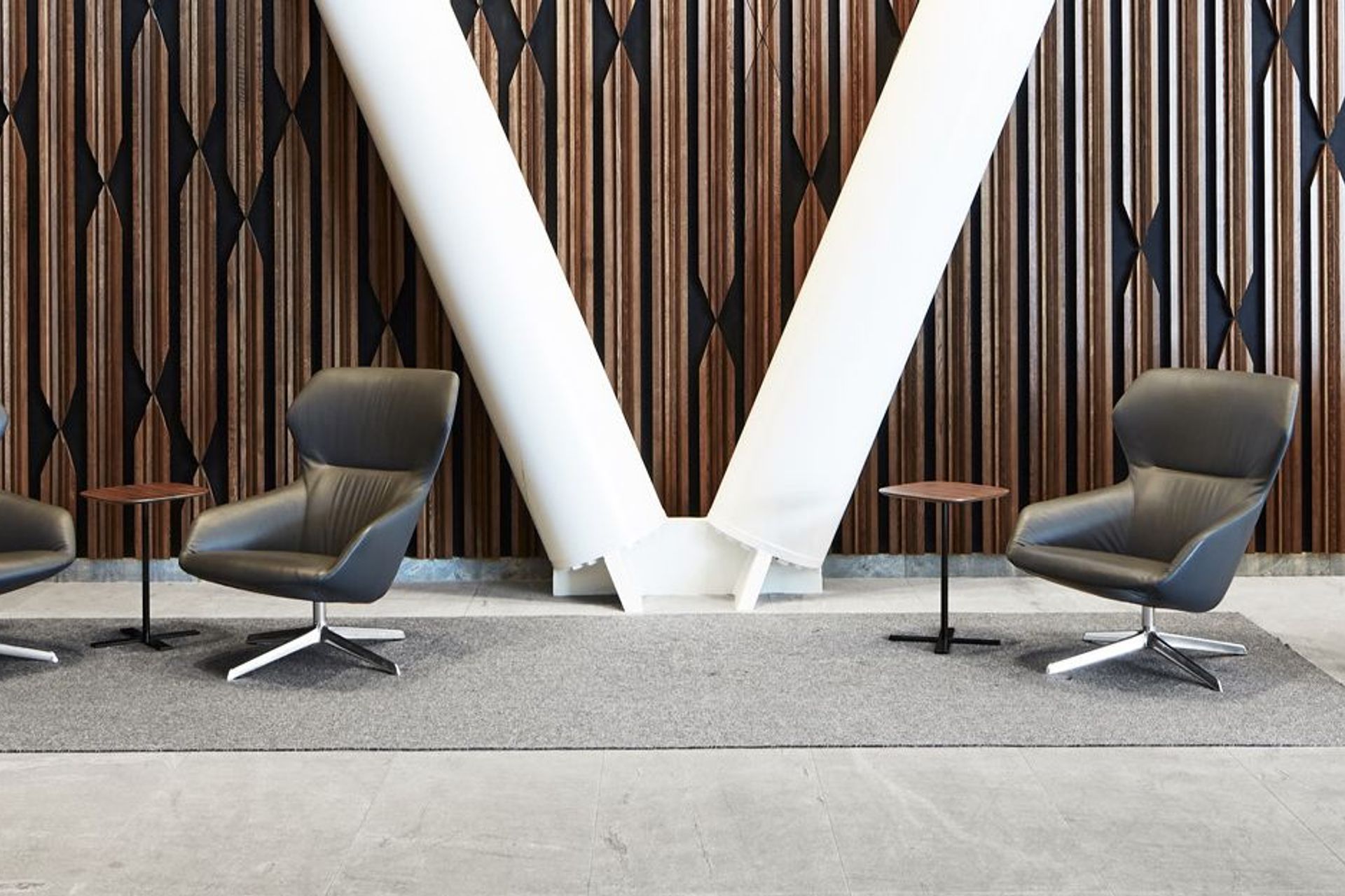The lobby of XXCQ utilises natural materials, with a timber-panelled feature wall, angular reception desk in polished stone and brass, and curvaceous Scandinavian-style leather-clad chairs.
