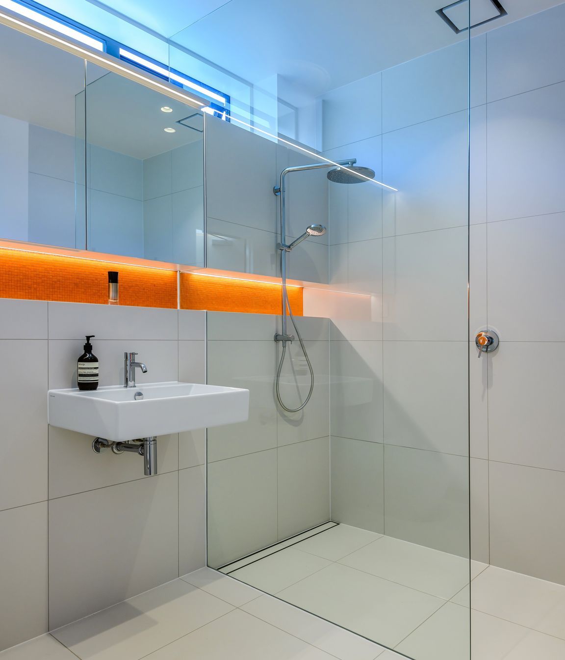 A pop of orange in the tiling and LED lighting elevate this otherwise all-white bathroom.