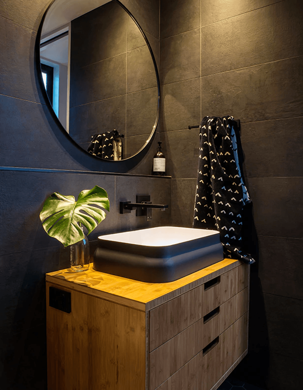 A round mirror, framed in black, is the perfect choice to bounce subtle light around the room while keeping with the theme.