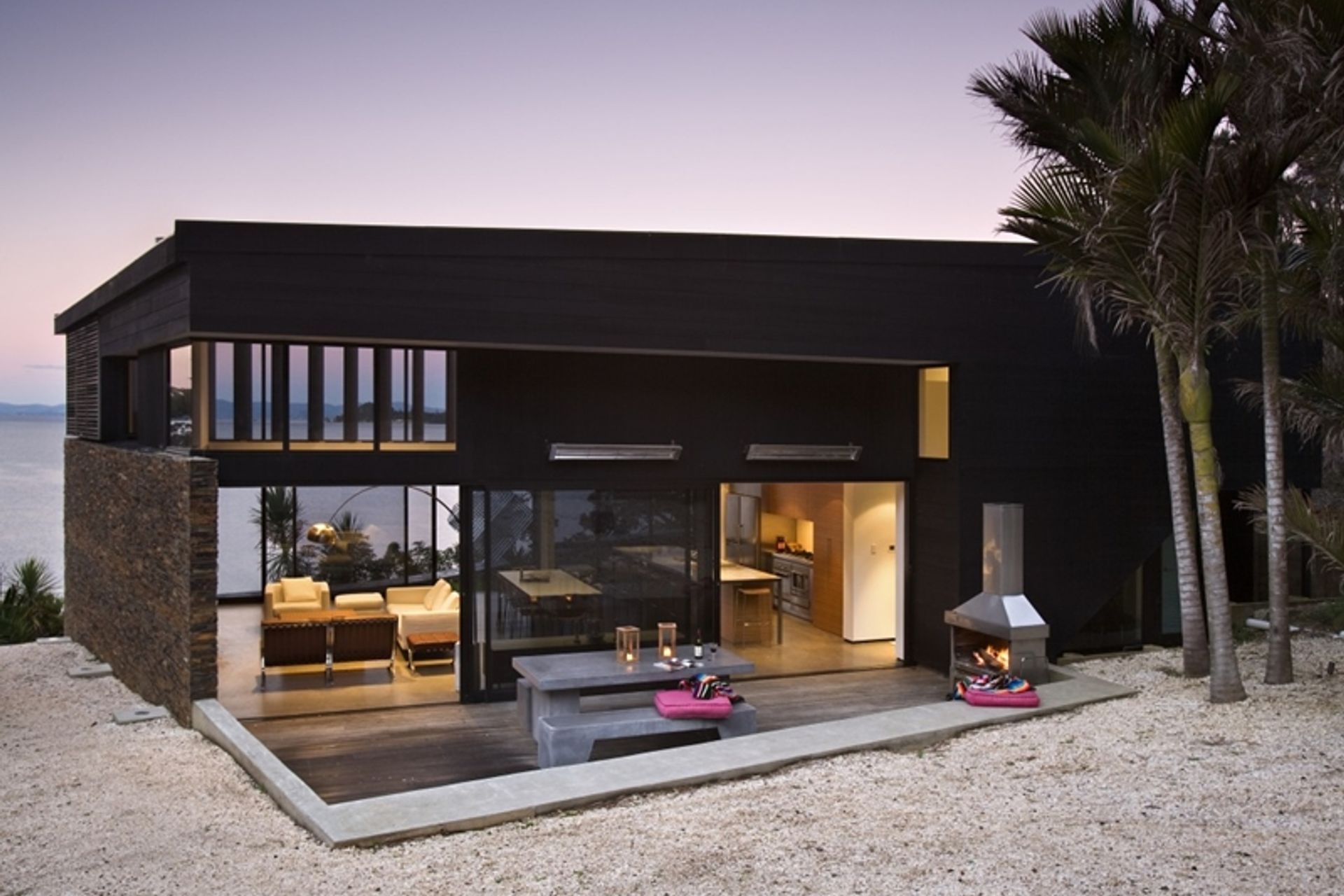 Bright outdoor cushions in the fuschia accent colour bring a holiday feel to this modern Waikopua beach house by Daniel Marshall Architects.