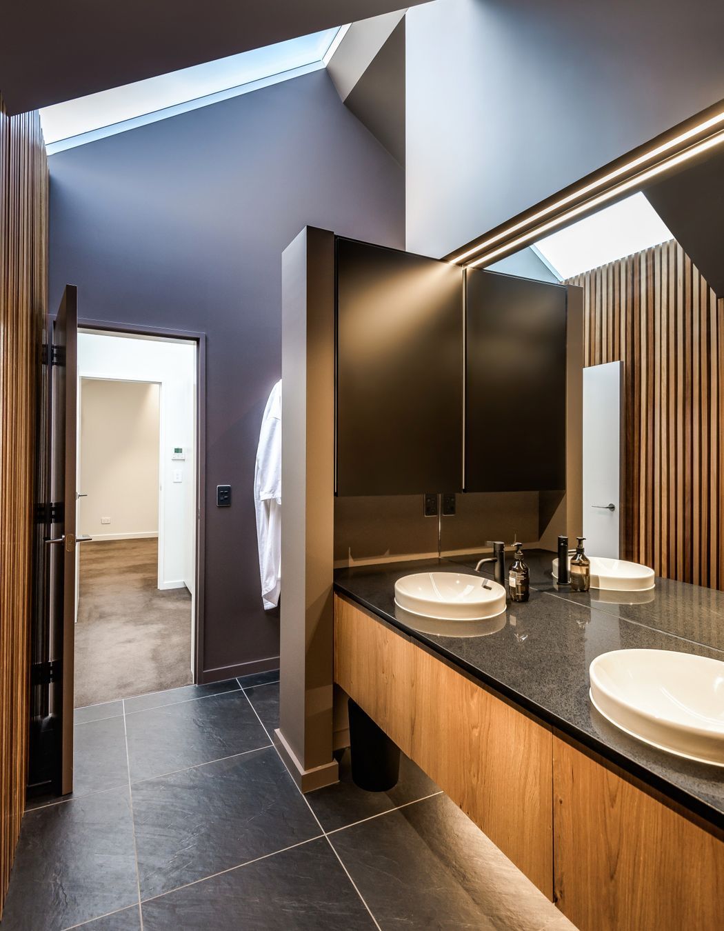 The bathroom uses large-format concrete-look tiles and timber cabinetry and panelling