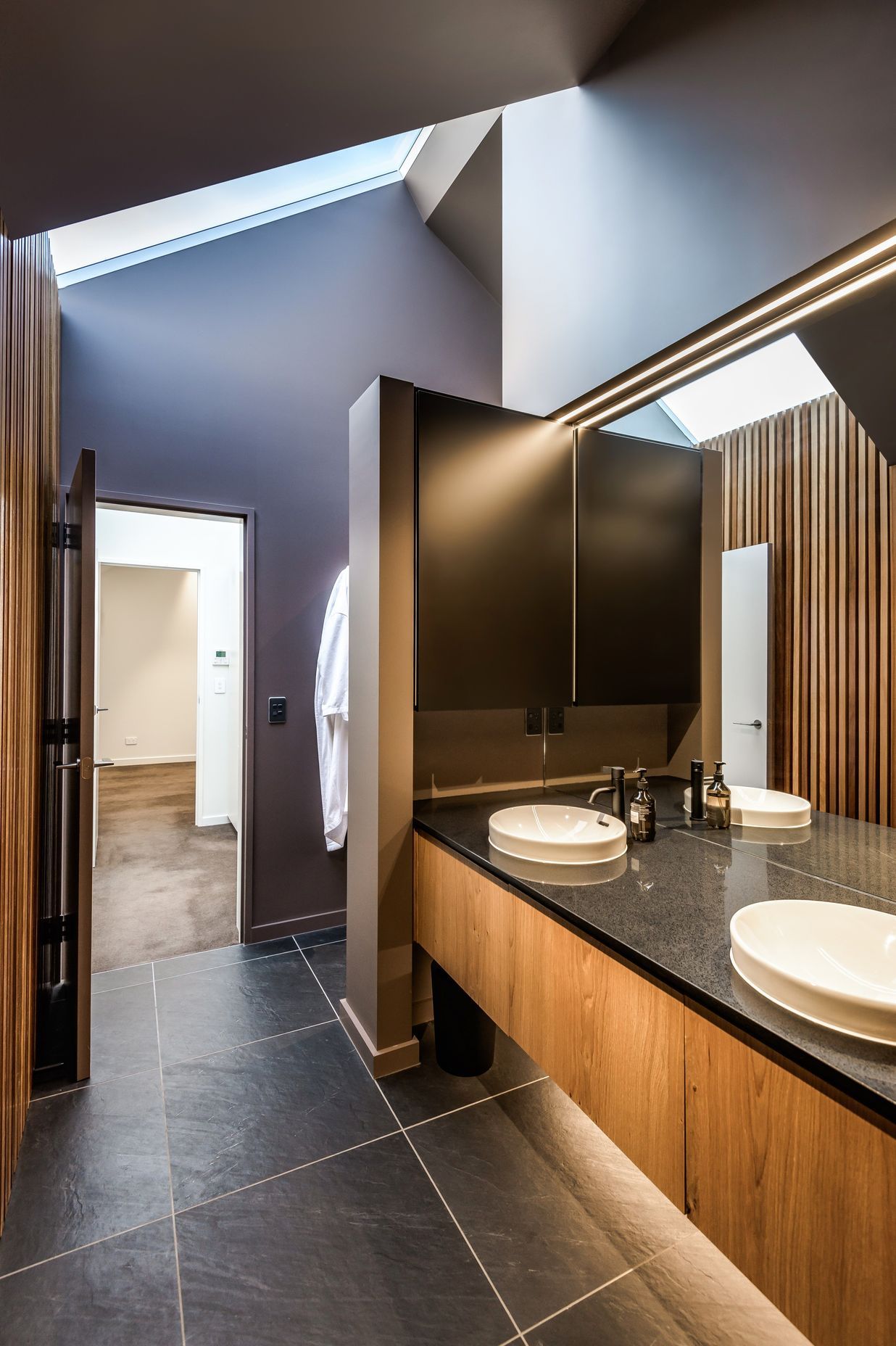 The bathroom uses large-format concrete-look tiles and timber cabinetry and panelling