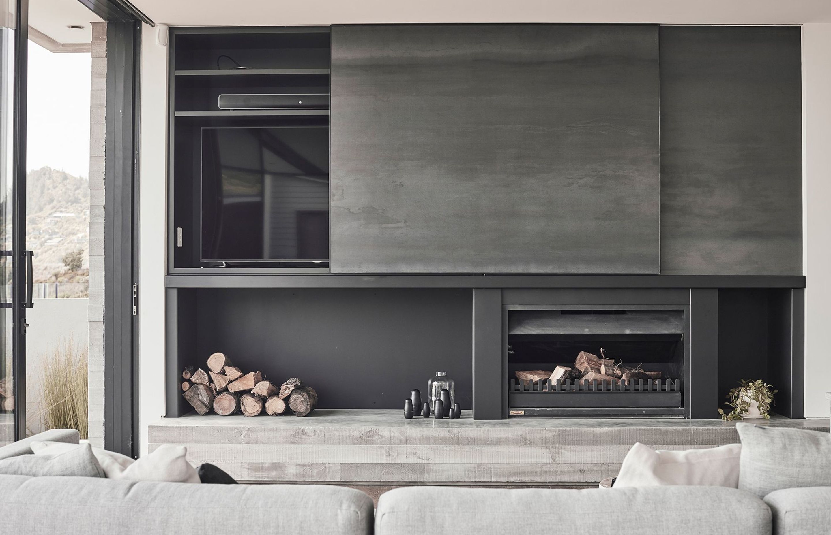 A woodburner atop an in situ concrete plinth provides warmth, surrounded by dark porcelain panels that create a depth and contrast to the stark whites of the kitchen.