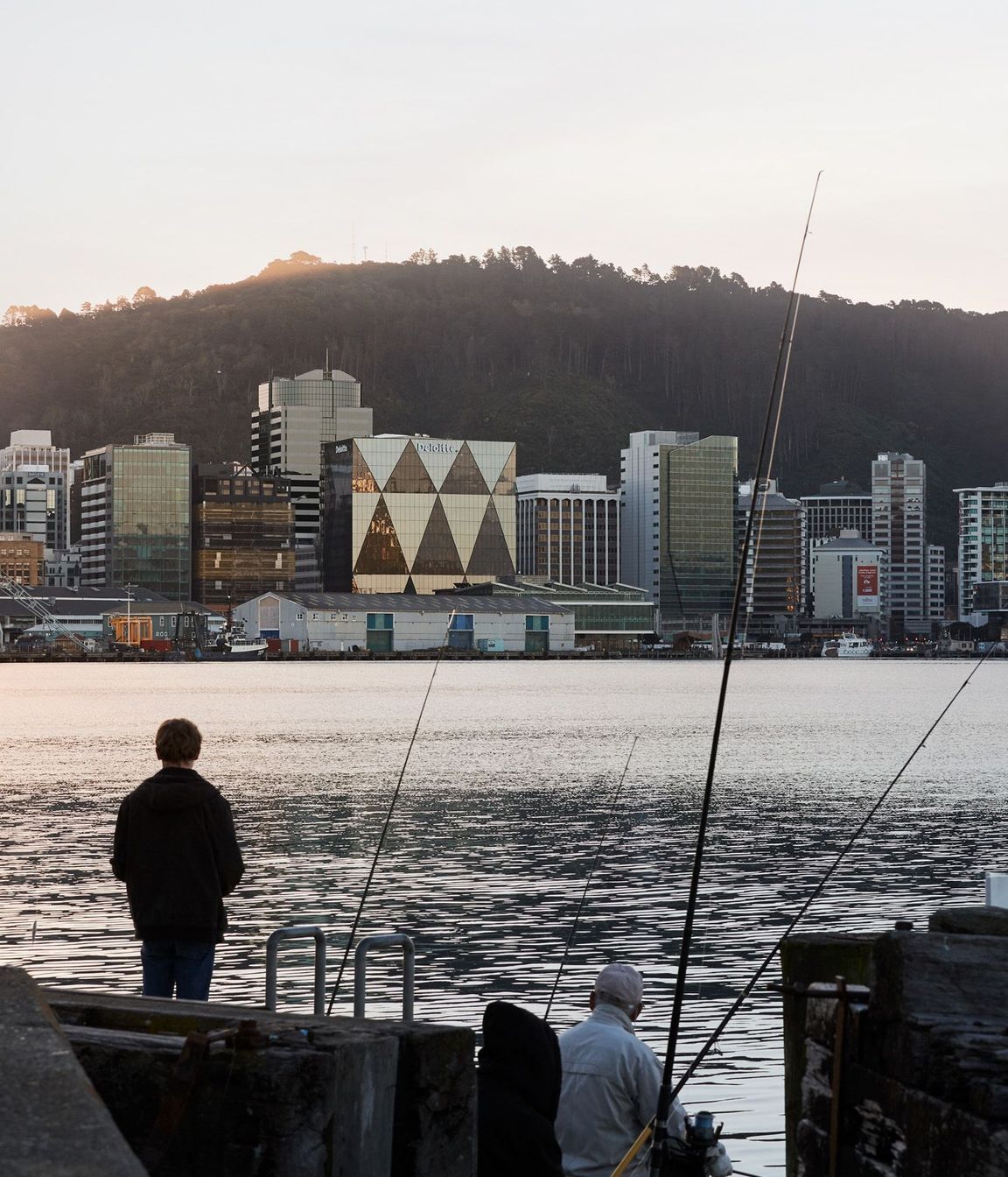 Fishermen enjoy the view from Oriental Parade of the XXCQ building, which reflects the afternoon sun.