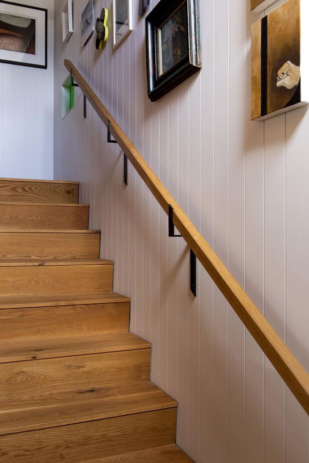 A narrow interior stairway with warm timber treads and a matching timber handrail. The stair wall is clad in vertically grooved painted wall panelling, with framed artwork and small recessed display niches along the ascent. The space is compact, warm, and thoughtfully detailed.