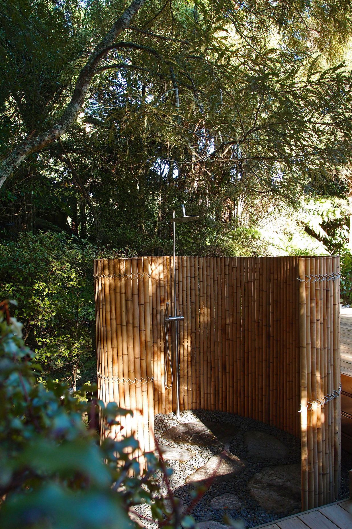 The outdoor shower is enclosed by a bamboo screen in a spiral. The floor is smooth schist and rounded pebble.