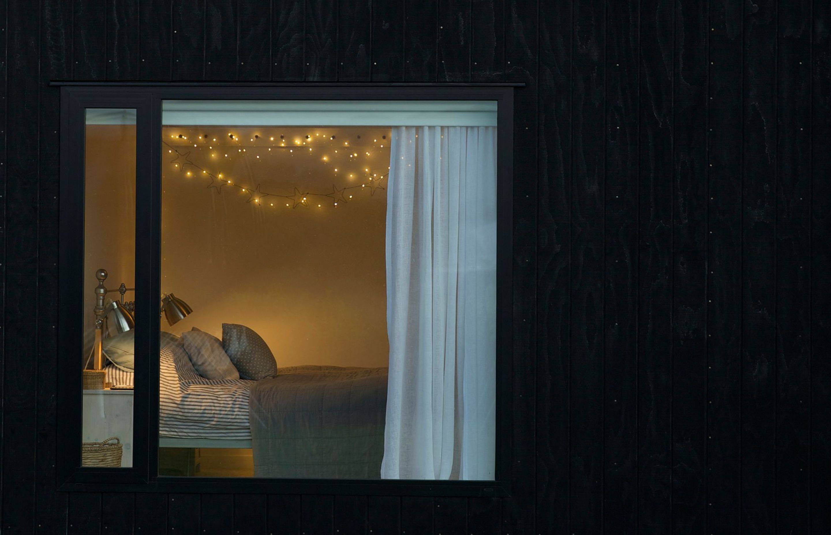 Black grooved plywood shadowcladding forms the perfect frame for the windows, carefully positioned to frame the views. At dusk, here, the bedroom lighting creates a warm glow.